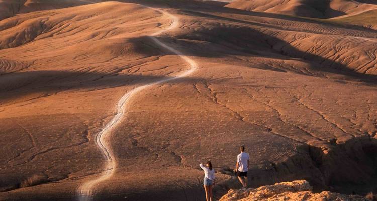 Twee wandelaars bekijken glooiende okerkleurige woestijnheuvels onder warm avondlicht