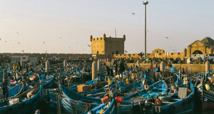 Haven vol met blauwe vissersboten naast stenen fort in Essaouira
