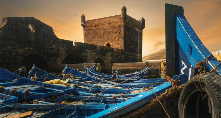 Dramatische zonsondergang boven stenen fort en doolhof van blauwe boten in de haven van Essaouira