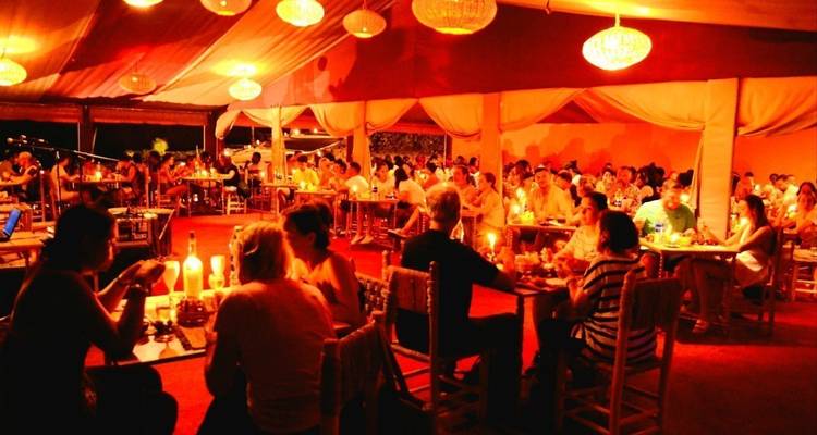 Groot tentrestaurant verlicht door warme lantaarns met gasten aan tafels bij kaarslicht