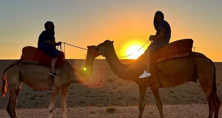 Silhouetten van kameelruiters tegen een levendige woestijnzonsondergang