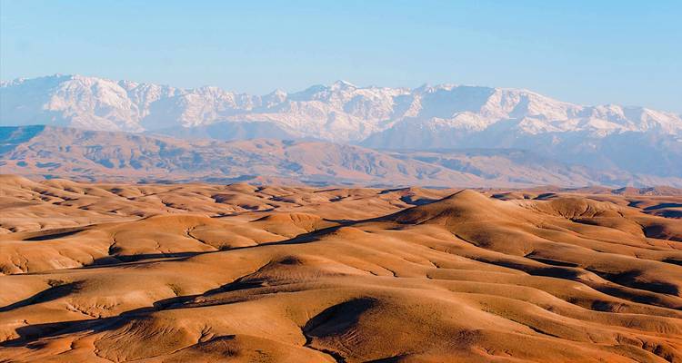 Weids uitzicht over okerkleurige woestijnduinen met besneeuwde Atlasgebergte erachter