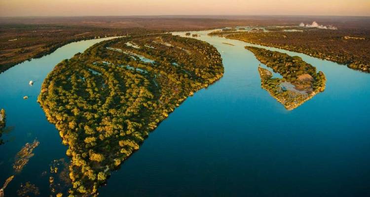 Îles serpentines couvertes de forêts luxuriantes serpentant à travers les eaux bleu profond du fleuve Zambèze à l'heure dorée.