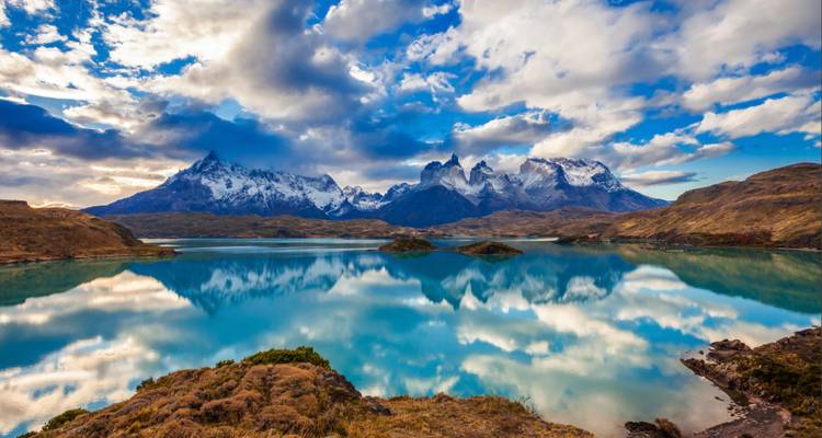 Dramatische zerklüftete Gipfel der Torres del Paine spiegeln sich perfekt in einem türkisfarbenen See unter einem Himmel voller aufquellender Wolken wider.