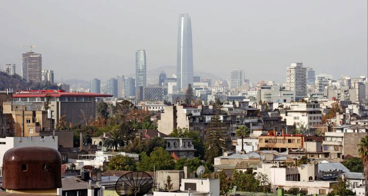 Moderne Skyline von Santiago, dominiert von einem hohen Glasturm, der sich über eine dichte städtische Bebauung erhebt.
