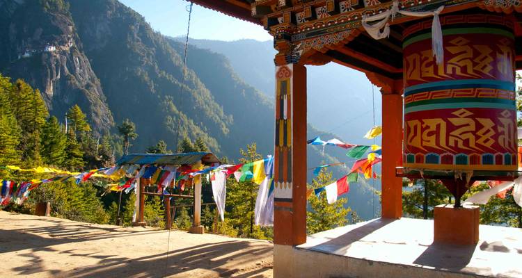Banderas de oración coloridas y rueda de oración ornamentada con vista a un valle boscoso