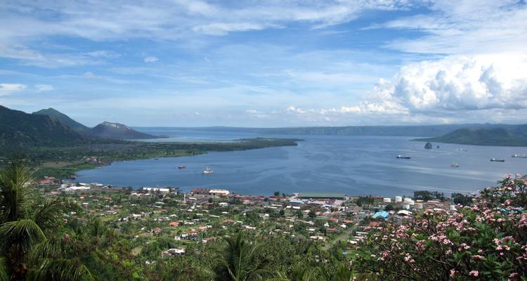 Vista panorámica sobre un pueblo costero y una amplia bahía con nubes dispersas y colinas distantes