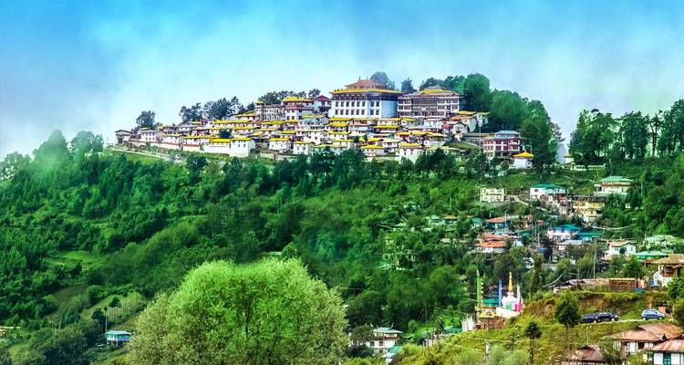 Espectacular complejo monasterial en la cima de una colina con vistas a laderas boscosas verdes y pueblos.