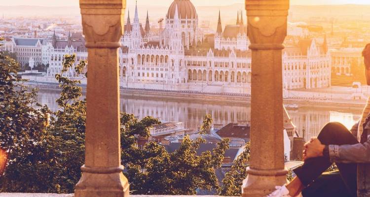 Abendliche Stadtansicht des Parlamentsgebäudes von Budapest durch die Säulen der Fischerbastei mit einem einzelnen Besucher.