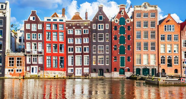 Maisons de canal emblématiques et étroites se reflétant dans l'eau sous un ciel bleu éclatant à Amsterdam