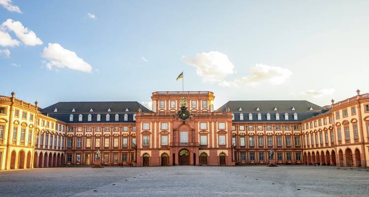 Symmetrische Fassade des Mannheimer Barockschlosses, die im späten Nachmittagslicht vor blassem Himmel leuchtet.