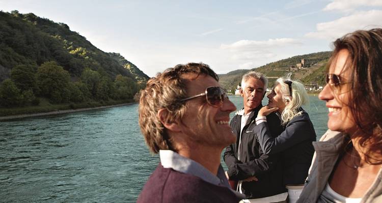 Grupo de viajeros maduros disfrutando de un crucero fluvial con colinas cubiertas de viñedos al fondo.