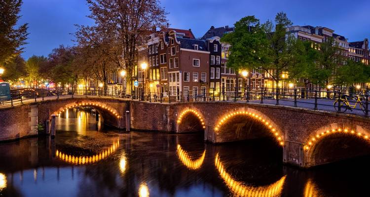 Les lumières scintillantes d'un pont de briques voûté au-dessus du canal nocturne tranquille d'Amsterdam