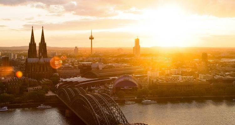 Sunset over Cologne with the cathedral, TV tower and Hohenzollern Bridge glowing above the Rhine.