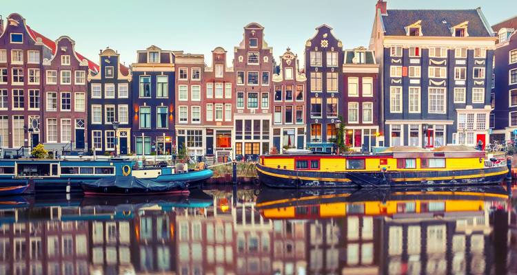 Rangée emblématique de maisons colorées du canal se reflétant dans l'eau calme à l'aube à Amsterdam.