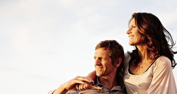Portrait rapproché d'un couple souriant s'embrassant contre un ciel doré à la lumière douce.