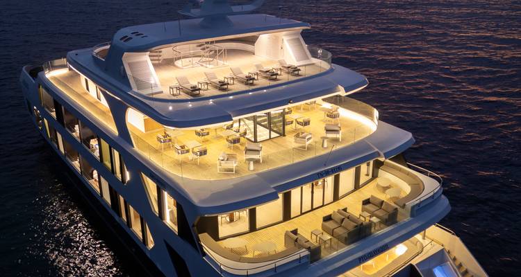Illuminated luxury expedition yacht decked with lounge chairs gliding over deep blue ocean at dusk.