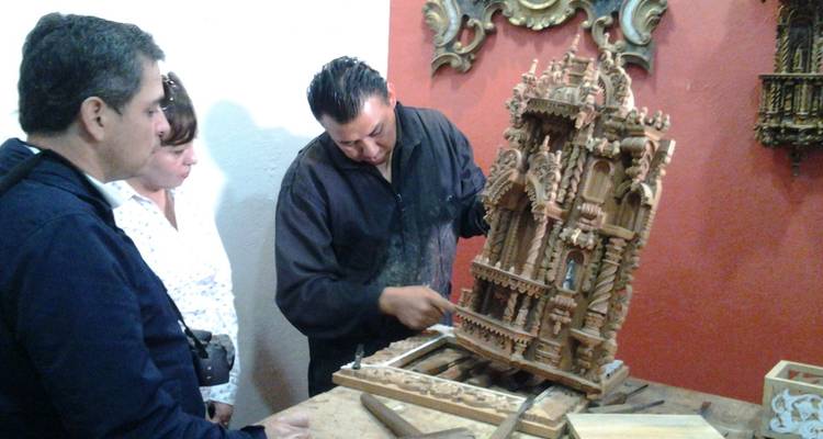 Skilled artisan carving an intricate wooden altarpiece while visitors observe closely.