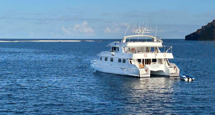 Weißer Katamaran vor Anker in den klaren blauen Gewässern der Galapagos mit kleinem Beiboot in der Nähe.