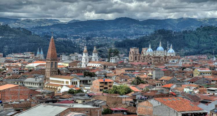 Dachpanorama der Stadt Cuenca mit historischen Kirchen vor bewaldeten Hügeln unter dramatischen Wolken.