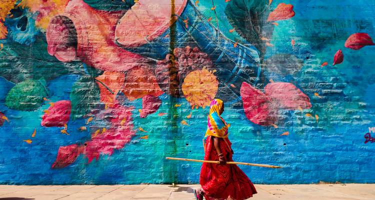 A brightly dressed woman walks past a colorful street mural in India.