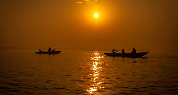 Silhouetted rowboats float on a golden river beneath a rising sun.