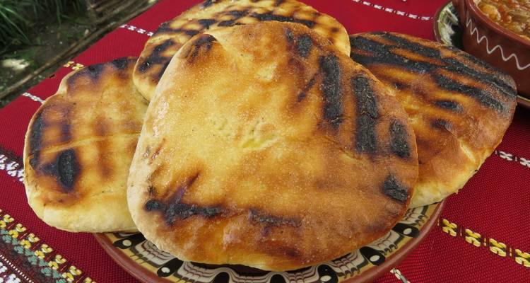 Panes planos búlgaros a la parrilla con marcas de carbón servidos en un plato con diseño tradicional.