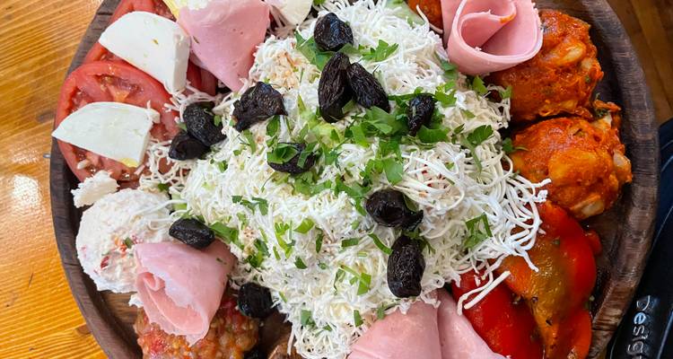 Abundante plato de madera con ensalada Shopska, carnes, quesos y aceitunas.