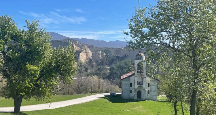 Pintoresca iglesia rural y acantilados de las pirámides de arena de Melnik enmarcados por árboles en flor en una mañana de primavera.