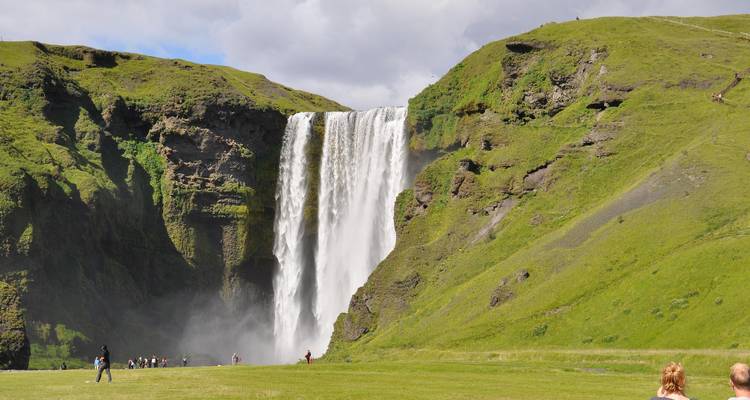 Besucher stehen vor dem mächtigen Skogafoss-Wasserfall, der in den Nebel stürzt.