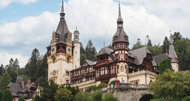 Sprookjesachtig kasteel Peles omringd door beboste heuvels onder een gedeeltelijk bewolkte hemel
