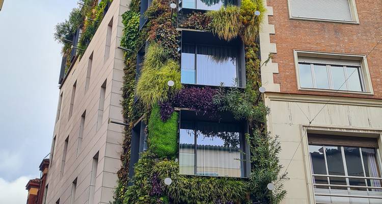 Edificio urbano moderno cubierto de exuberantes jardines verticales y ventanas reflectantes en un día nublado.