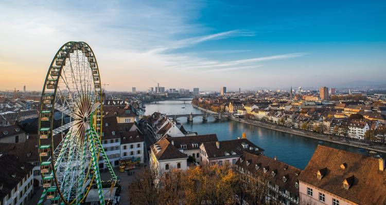 Grande roue surplombant les toits de Bâle et le Rhin au coucher du soleil.