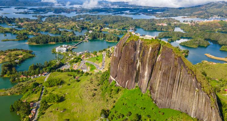 Aerial of towering El Peñol rock surrounded by blue lakes and green hills near Medellín.