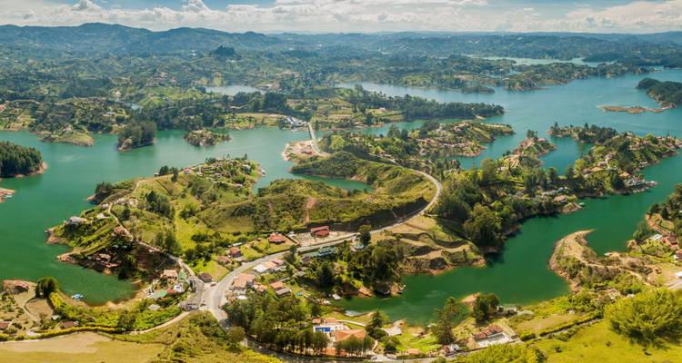Panoramic drone view of Guatapé’s emerald reservoir dotted with green islands and rolling hills under a bright sky.