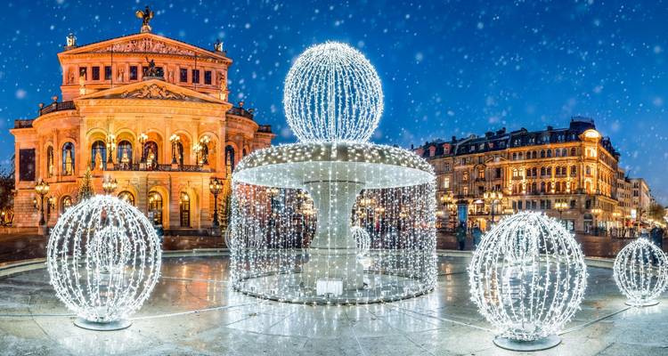 Escena nocturna de la Alte Oper de Frankfurt con decoraciones de fuentes esféricas luminosas bajo una suave nevada.
