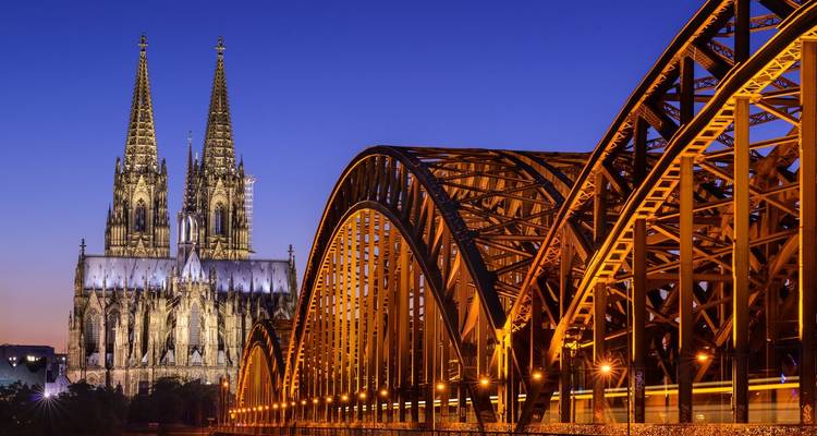 La cathédrale emblématique de Cologne à côté du pont ferroviaire illuminé de Hohenzollern sur le Rhin à l'heure bleue.