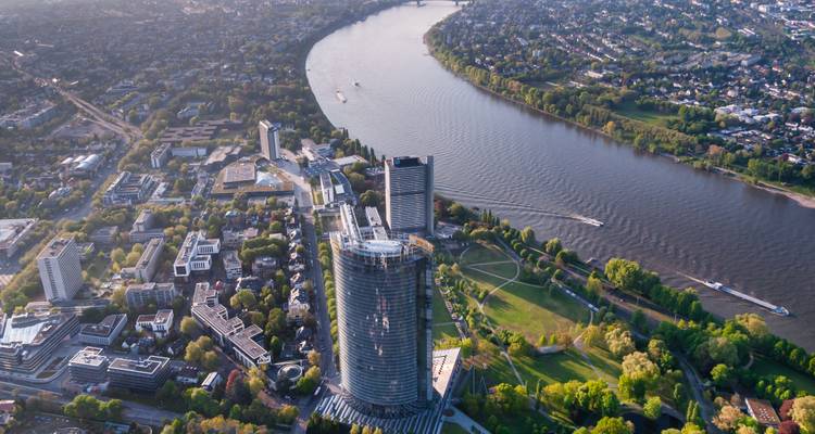 Vue aérienne de Bonn montrant le Rhin sinueux, le gratte-ciel Post Tower et les parcs verts des berges sous un ciel dégagé.