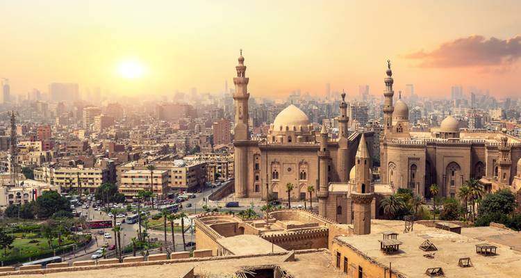 Panorama del atardecer sobre El Cairo con la Mezquita del Sultán Hassan y el horizonte de la ciudad resplandeciendo bajo una luz dorada.