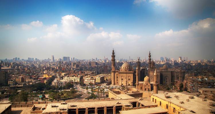 Panorama expansivo de El Cairo con los minaretes gemelos de la Mezquita del Sultán Hassan prominentes contra un horizonte brumoso.