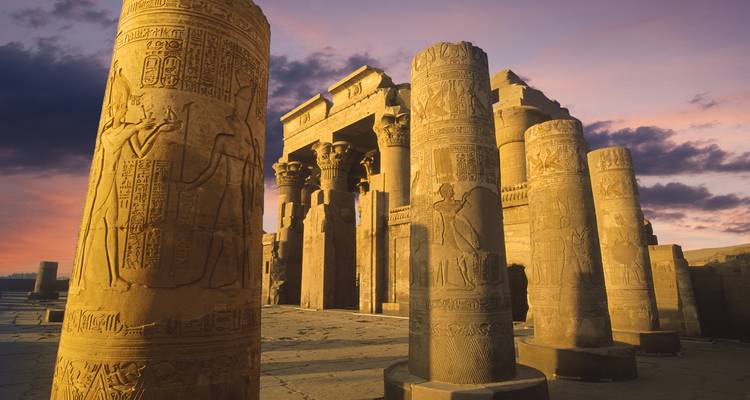 Des colonnes richement sculptées et l'entrée du temple de Kom Ombo brillent sous un ciel coloré du soir.