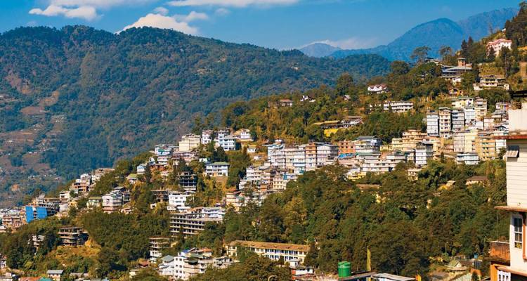 Weite Ansicht einer terrassenförmig angelegten Bergstadt in Sikkim, umgeben von bewaldeten Hängen and blauen Bergen.