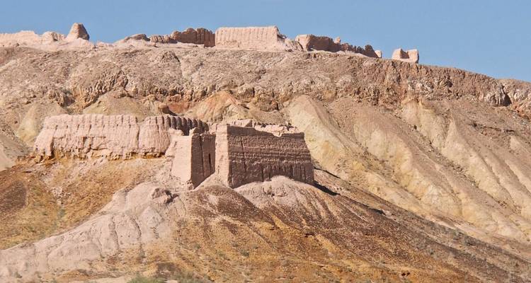 Lehmziegel-Festungsruinen krönen einen gestreiften Wüstengrat unter einem klaren blauen Himmel.