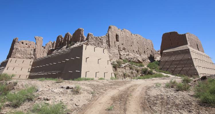 Bröckelnde Erdwälle einer Wüstenfestung stehen gegen einen strahlend blauen Himmel neben einem staubigen Pfad.