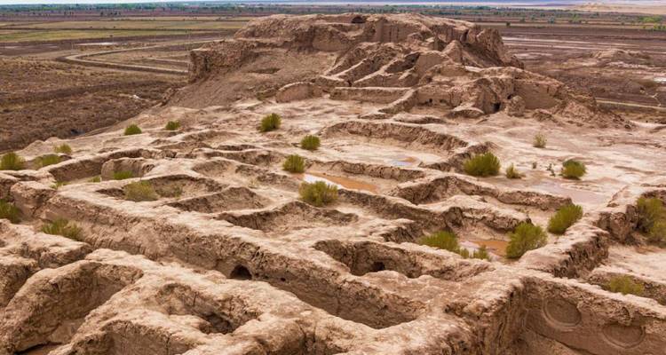 Ein erodiertes Labyrinth aus antiken Lehmziegelfundamenten erstreckt sich über eine karge Ebene.