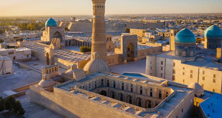Luftaufnahme bei Sonnenuntergang von Buchara mit dem hochragenden Kalyan-Minarett und blau gefliesten Madrasa-Kuppeln.