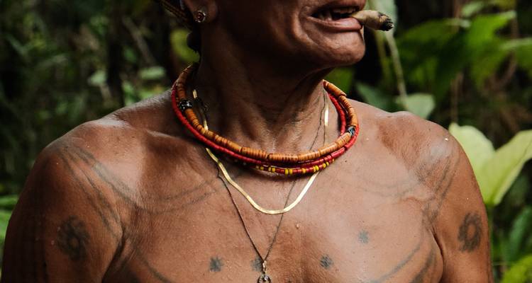 Portrait rapproché d'un ancien Mentawai avec des tatouages corporels et un cigare dans un cadre de jungle luxuriante.