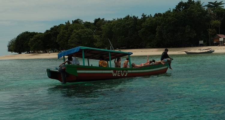 Un bateau en bois vert transporte des touristes sur une eau turquoise claire vers une plage d'île sableuse.