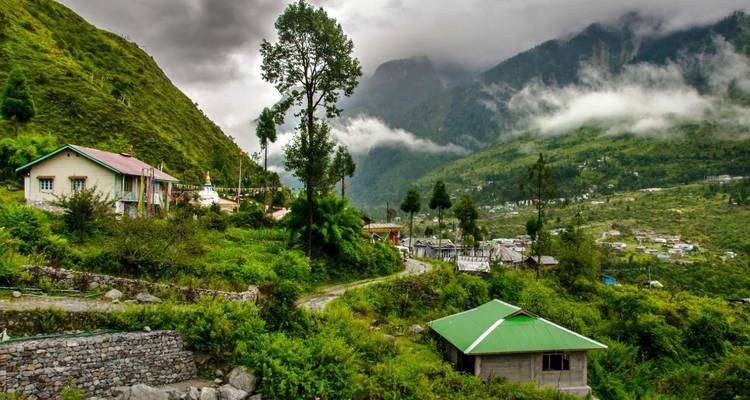 Misty green valley dotted with homes, winding path, and clouds hugging the forested peaks.