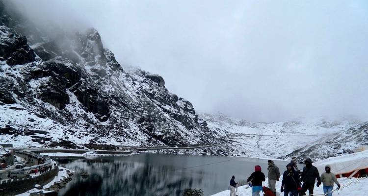 Snow-fringed alpine lake surrounded by steep rocky slopes with visitors playing near the shoreline.